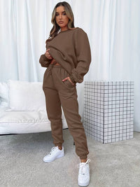 Frau in braunem Jogginganzug, weiße Sneaker, modernes Wohnzimmer, gemütliche Mode.