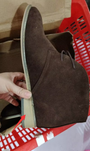 Brauner Wildlederstiefel mit flachem Absatz, handgehalten, in rotem Einkaufskorb.