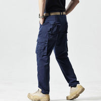 Mann in blauer Cargohose und beigen Wanderschuhen, seitlich stehend, auf hellem Hintergrund.