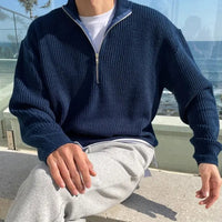Mann in dunkelblauem Strickpullover mit Reißverschluss, sitzt draußen, lässige Mode.