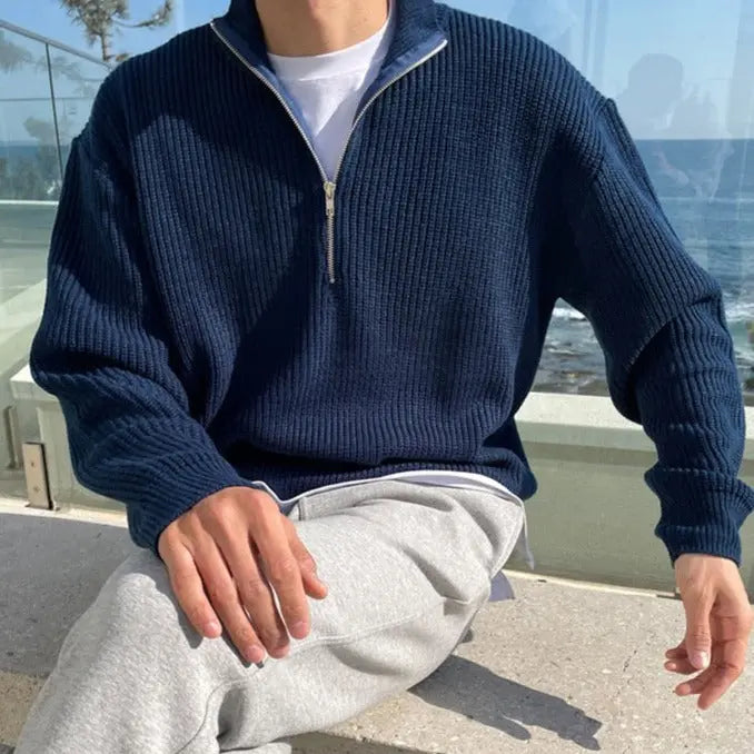 Mann in dunkelblauem Strickpullover mit Reißverschluss, sitzt draußen, lässige Mode.