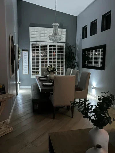 Elegantes Esszimmer mit Holztisch, grauen Stühlen, Kronleuchter und großen Fenstern bei Nacht.