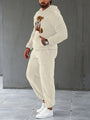 Mann in cremefarbenem Teddyfleece-Trainingsanzug mit Bärenmotiv, weiße Sneaker.