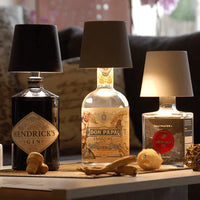 Drei Flaschenlampen aus Gin- und Rumflaschen mit schwarzen Lampenschirmen auf Holztisch.