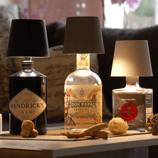 Drei Flaschenlampen aus Gin- und Rumflaschen mit schwarzen Lampenschirmen auf Holztisch.