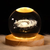 Leuchtende Kristallkugel mit Galaxie-Design auf Holzsockel, dekorative LED-Lampe.