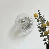 Glasvase mit Metallknauf, transparent, dekorativ, neben gelben Blumen und Eukalyptuszweigen.