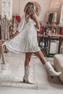 Frau im silbernen Paillettenkleid und weißen Cowboystiefeln in Boutique.
