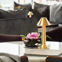 Goldene Tischlampe aus Metall neben rosa Blume auf modernem Wohnzimmertisch.