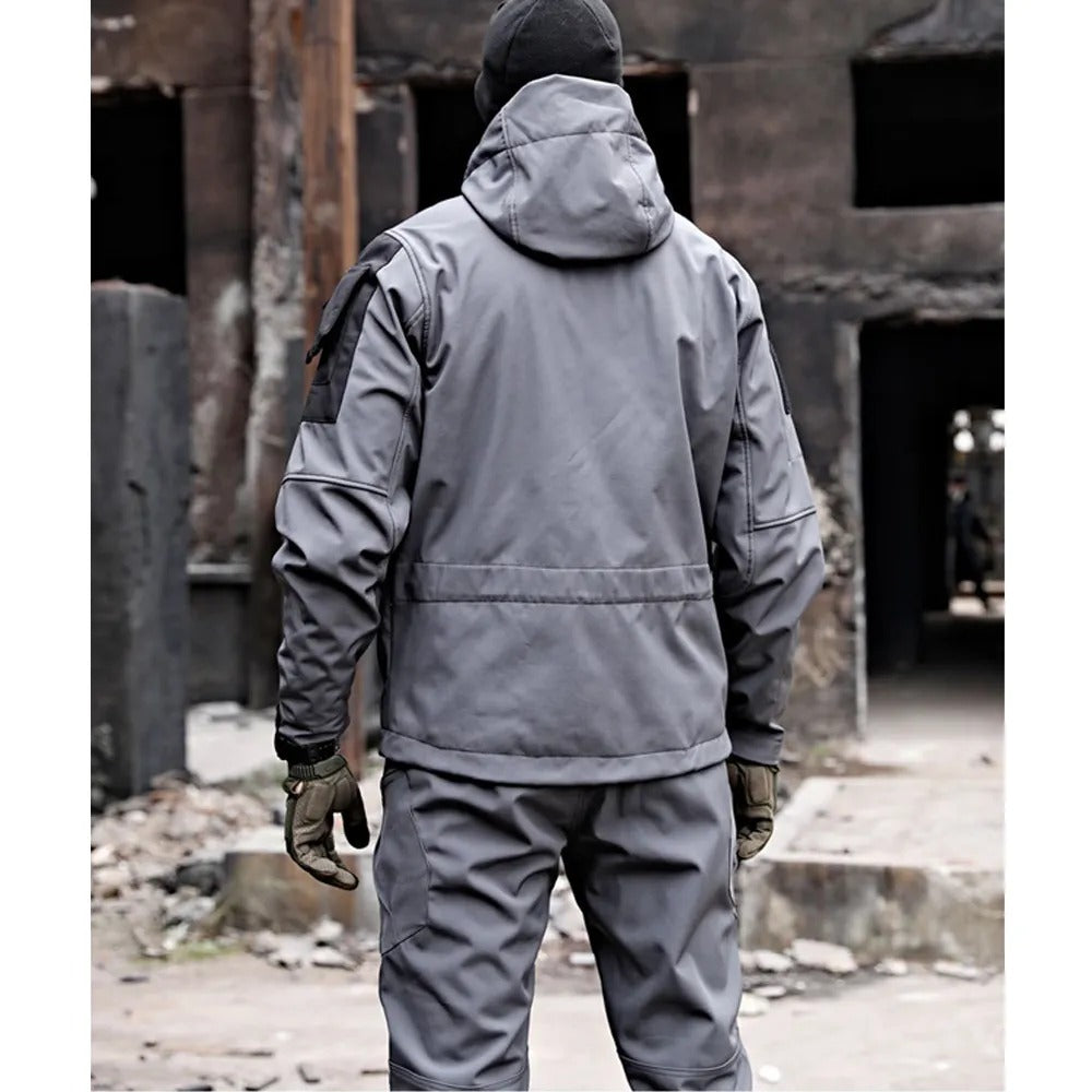 Mann in grauer taktischer Jacke und Hose, Outdoor-Bekleidung, urbaner Hintergrund.