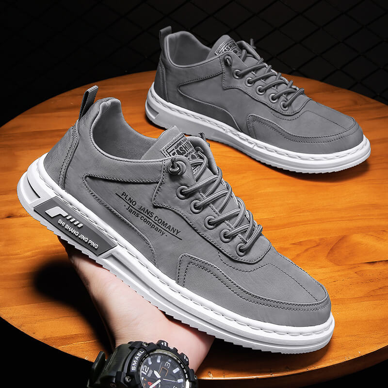 Graue Herrensneaker aus Leder mit weißer Sohle, modisches Design, auf Holztisch.