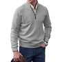 Mann in grauem Pullover mit Reißverschluss, Hemd, Jeans, Uhr, hält braune Jacke.