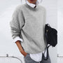 Frau in grauem Pullover, weißem Hemd, hält schwarze Tasche, lässiger Herbstlook.