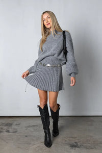 Frau in grauem Strickpullover und Rock, schwarze Stiefel, modisches Outfit, Herbstmode.