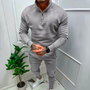 Mann in grauem Trainingsanzug mit Reißverschluss, weiße Sneaker, Zimmerpflanze, moderne Einrichtung.