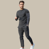 Mann in grauem Freizeitanzug mit Sonnenbrille und weißen Sneakers vor beigem Hintergrund.