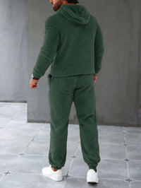 Mann in grünem Fleece-Trainingsanzug, Kapuze, weiße Sneaker, gemütliche Freizeitmode.