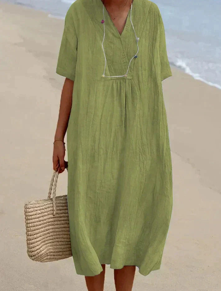 Frau in grünem Leinenkleid am Strand mit Strohtasche, Sommermode, lässiger Stil.
