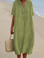 Frau in grünem Leinenkleid am Strand mit Strohtasche, Sommermode, lässiger Stil.