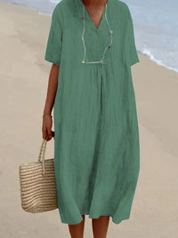 Frau im grünen Leinenkleid am Strand mit Strohtasche, Sommermode, lässiger Stil.