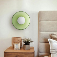 Grüne Wandleuchte im modernen Schlafzimmer, runde Form, neben Nachttisch mit Dekoration.