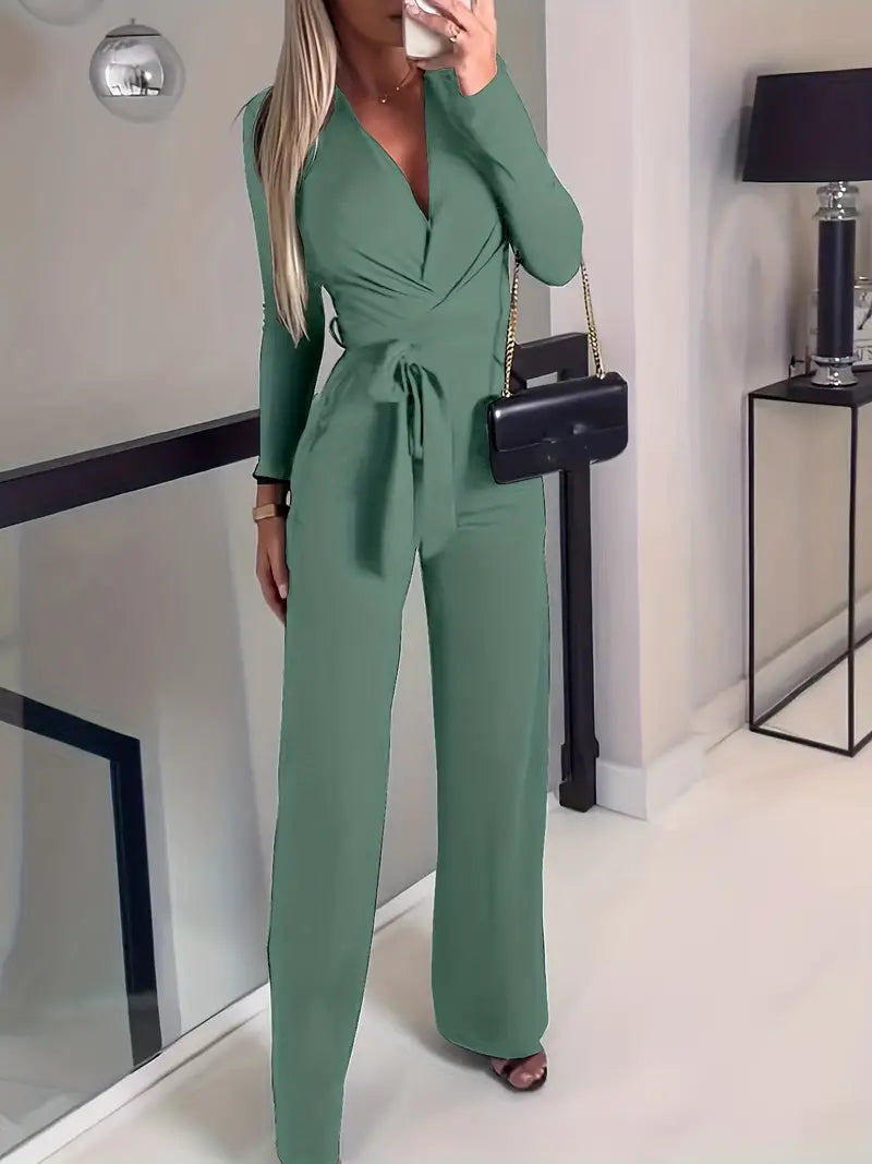 Frau in grünem Jumpsuit mit Gürtel, schwarze Umhängetasche, moderne Inneneinrichtung.