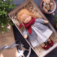 Handgemachte Waldorf-Puppe mit rotem Schal und grauem Mantel in Geschenkbox.