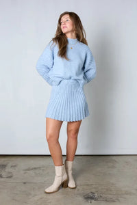 Frau in hellblauem Strickpullover und Rock, cremefarbene Stiefel, modisches Outfit.