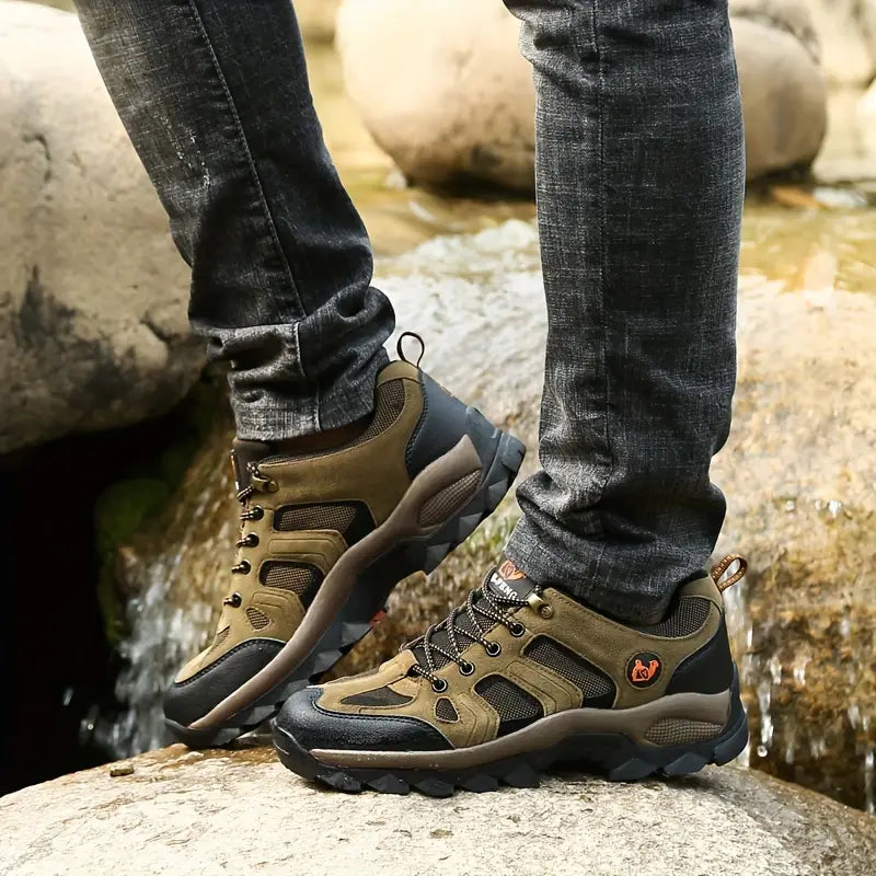 Person trägt olivgrüne Wanderschuhe, Outdoor, wasserdicht, robust, auf Felsen am Fluss.
