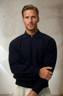 Mann in schwarzem Pullover mit Reißverschluss, modisch, elegant, vor neutralem Hintergrund.