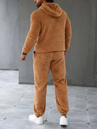Mann in braunem Teddy-Fleece-Trainingsanzug, Kapuzenjacke, Jogginghose, weiße Sneaker.