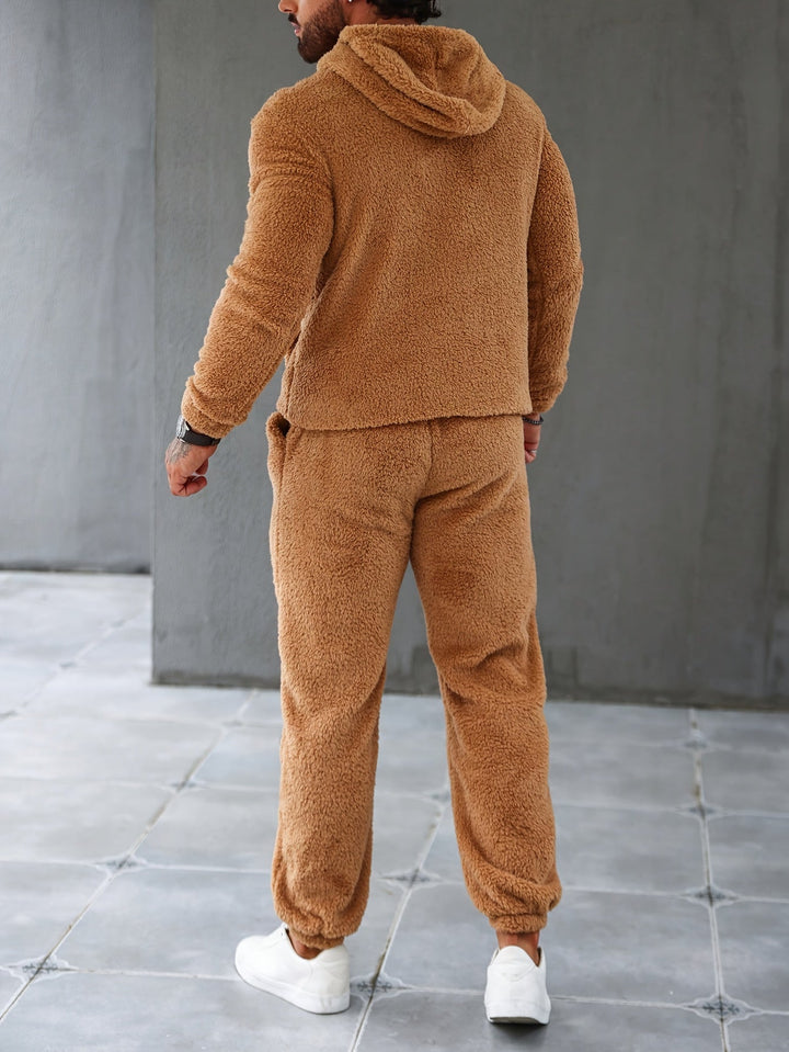 Mann in braunem Teddy-Fleece-Trainingsanzug, Kapuzenjacke, Jogginghose, weiße Sneaker.