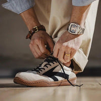 Mann bindet schwarze und weiße Sneaker, trägt Armbanduhr und beige Hose.