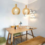 Esszimmer mit Holztisch, grünen Stühlen, hölzernen Pendelleuchten und geometrischer Wandlampe.