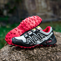 Grauer und roter Trailrunning-Schuh mit robustem Profil auf Felsen, ideal für Outdoor-Aktivitäten.