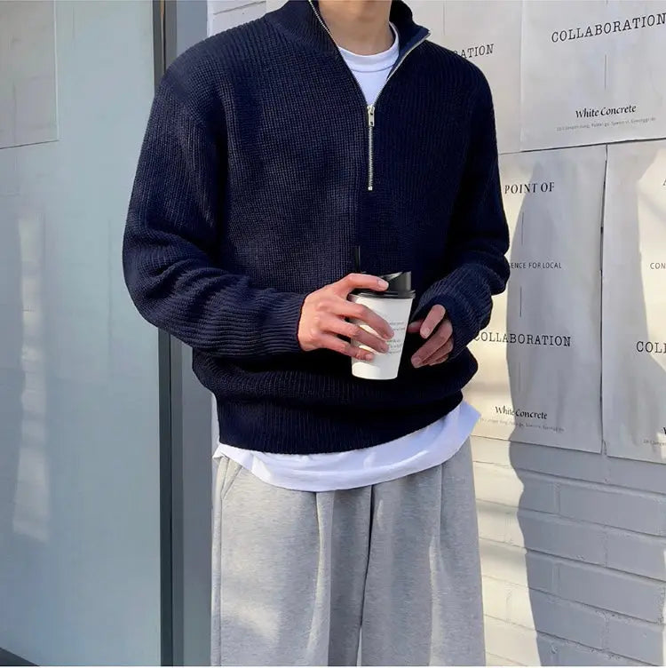 Mann in dunkelblauem Strickpullover mit Reißverschluss, hält weißen Kaffeebecher, lässige Mode.