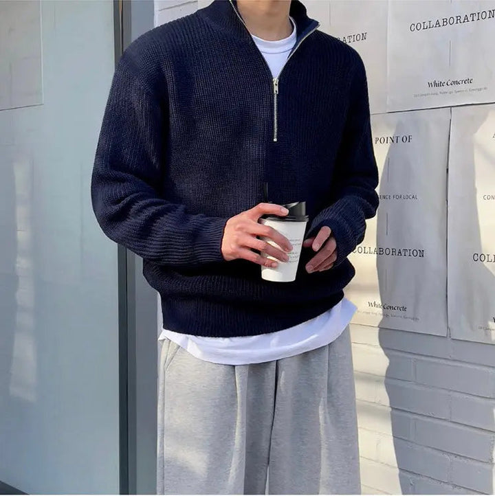 Mann in dunkelblauem Strickpullover mit Reißverschluss, hält weißen Kaffeebecher, lässige Mode.