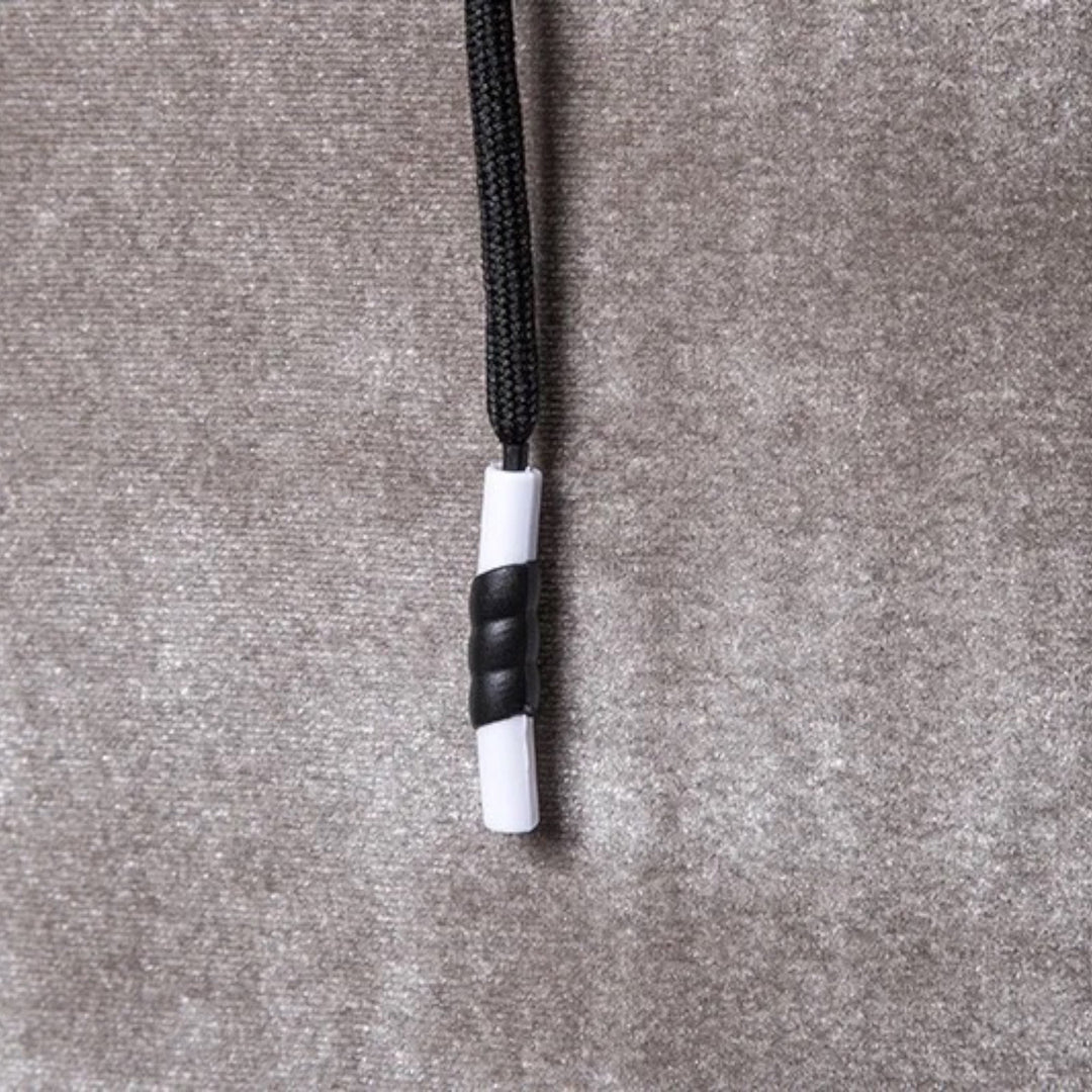 Schwarze und weiße Kordelstopper auf grauem Stoffhintergrund, Textilzubehör.