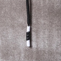 Schwarze und weiße Kordelstopper auf grauem Stoffhintergrund, Textilzubehör.