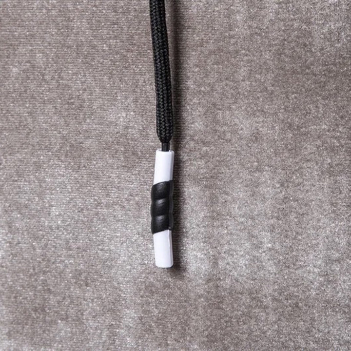Schwarze und weiße Kordelstopper auf grauem Stoffhintergrund, Textilzubehör.