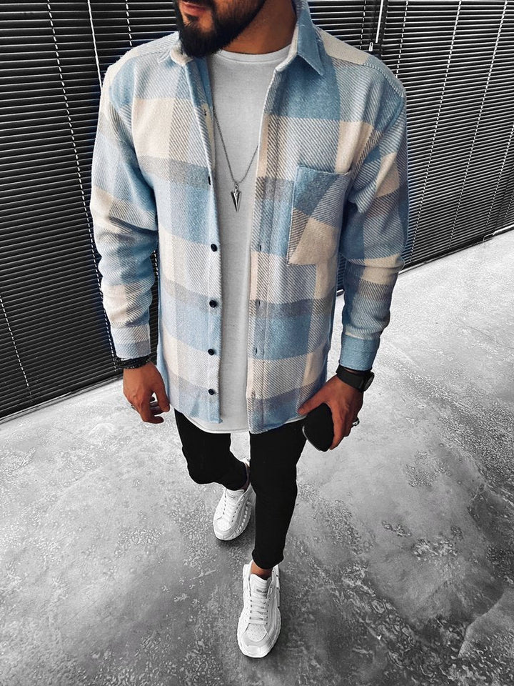 Mann in kariertem Hemd, weißem T-Shirt, schwarzer Hose und weißen Sneakers, modern gekleidet.