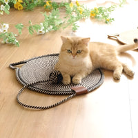 Goldene Katze auf gestreifter Katzenmatte aus Seil, umgeben von Blumen auf Holzboden.