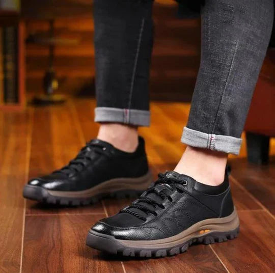 Schwarze Herren-Ledersneaker, rutschfeste Sohle, lässig, robust, auf Holzboden.