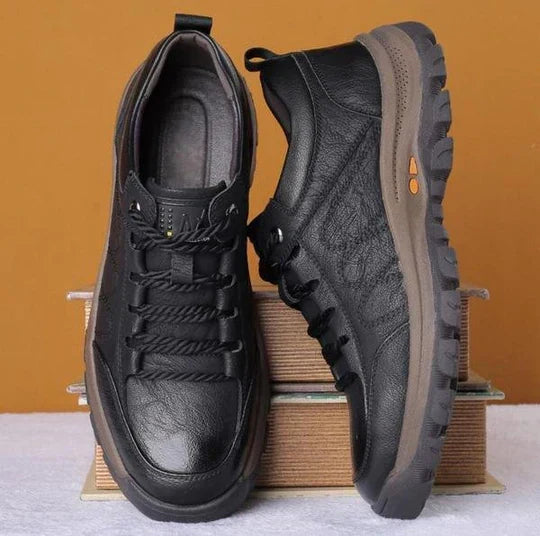 Schwarze Herren-Wanderschuhe aus Leder mit rutschfester Sohle auf Bücherstapel.