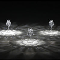 Drei kristallklare LED-Tischlampen mit facettiertem Schirm auf dunklem Hintergrund, elegantes Design.