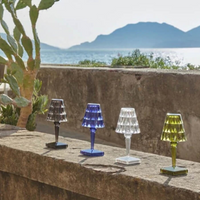 Vier bunte Kristall-Tischlampen auf Steinmauer vor Meer und Bergen im Hintergrund.