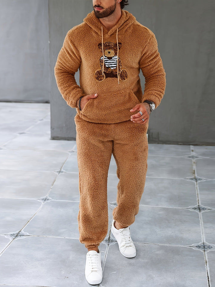 Mann in braunem Teddyfleece-Trainingsanzug mit Kapuze und Bärendesign, weiße Sneaker.