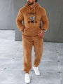 Mann in braunem Teddyfleece-Trainingsanzug mit Kapuze und Bärendesign, weiße Sneaker.