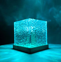 Leuchtender blauer Glaswürfel auf Holzsockel, dekorative Tischlampe, modernes Design.
