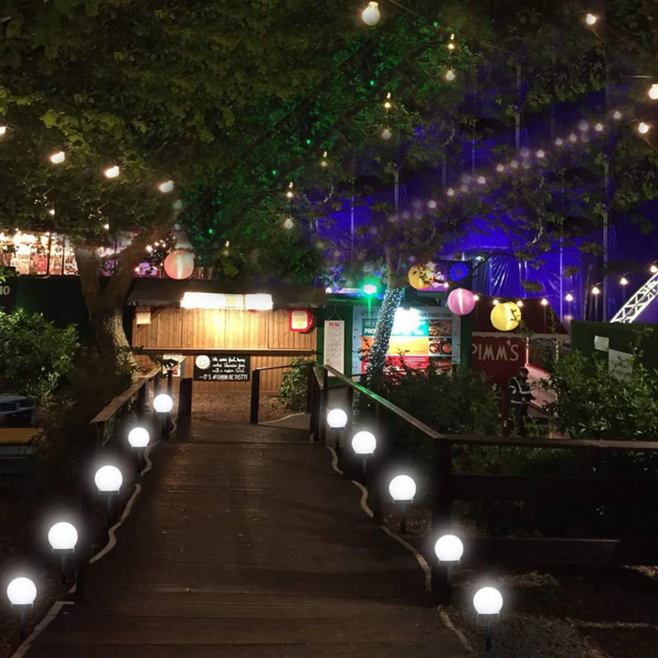 Festlich beleuchteter Gartenweg mit bunten Lichtern und Laternen, Nachtaufnahme.